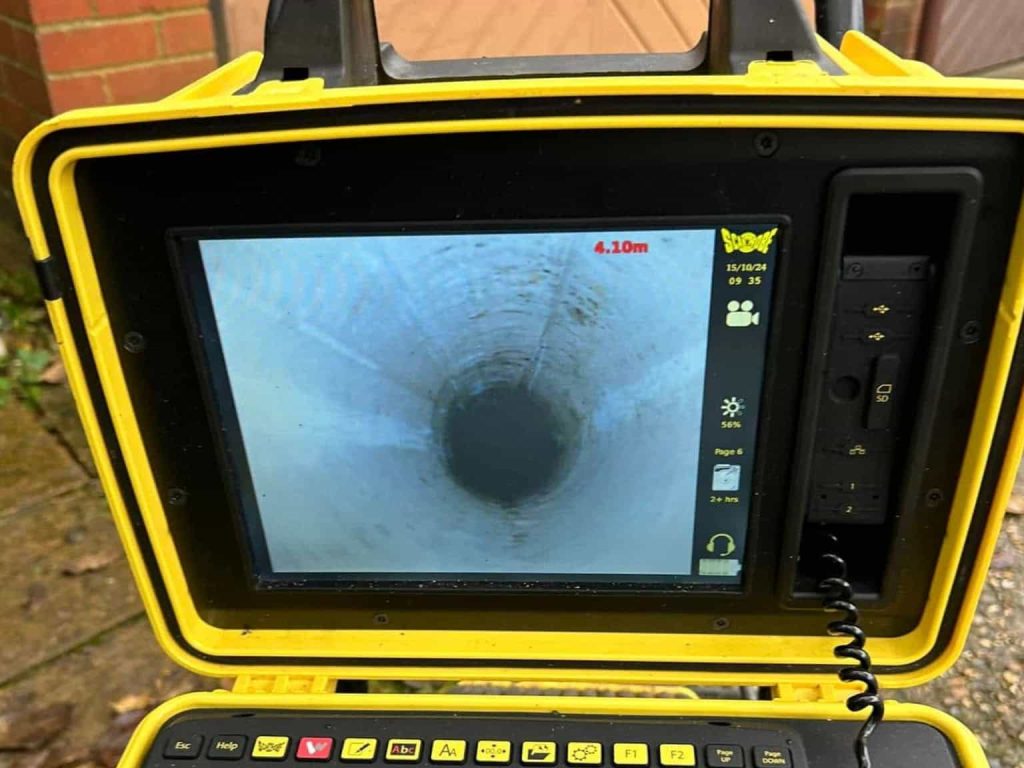 A close-up of a yellow inspection monitor displaying a live video feed of the inside of a pipe, showing a deep, circular tunnel view with distance marked as 4.10m on the screen.